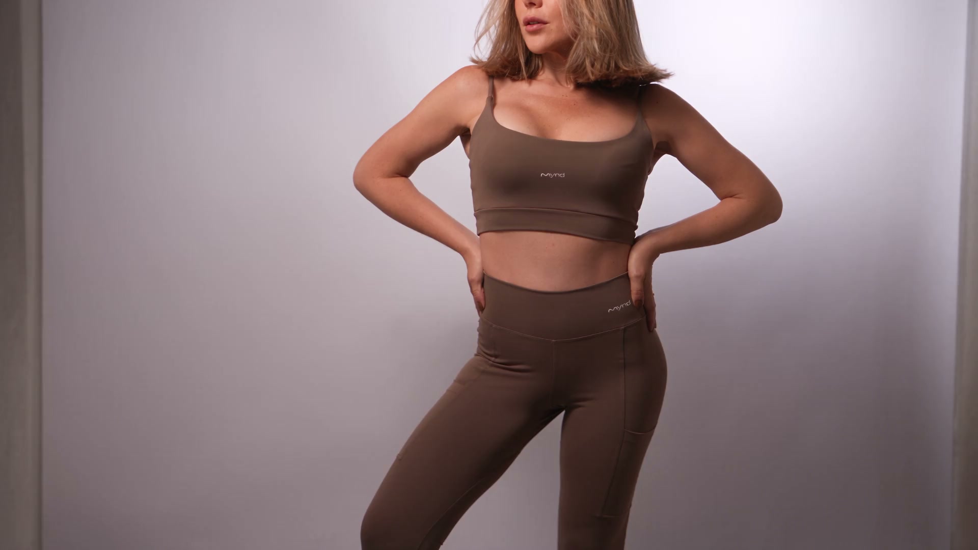 Modelo em estúdio usando o top e a legging Mynd marrom